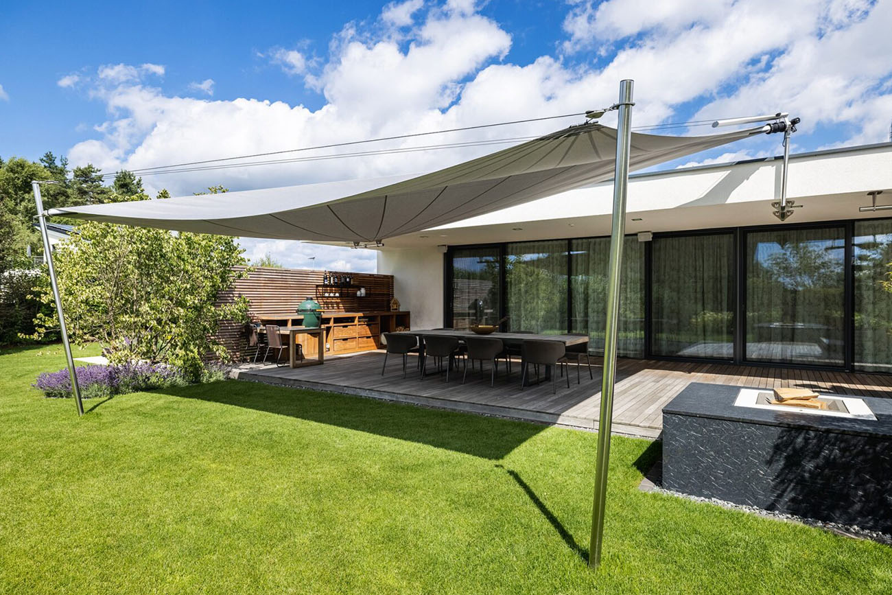 Sonnensegel für Villa mit Aussenküche in Zürich, am bestehenden Gebäude befestigt und Schraubanker im Terrain, 120 m² Segelfläche, Farbe: hellgrau, Funksteuerung steuerbar, windfest | wetterfest | UV-beständig, textiler Sonnen- und Wetterschutz für Privatbereich